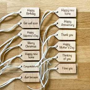 A set of personalized wooden gift tags with white string, printed with various birthday and holiday greetings, arranged on a light wood background.